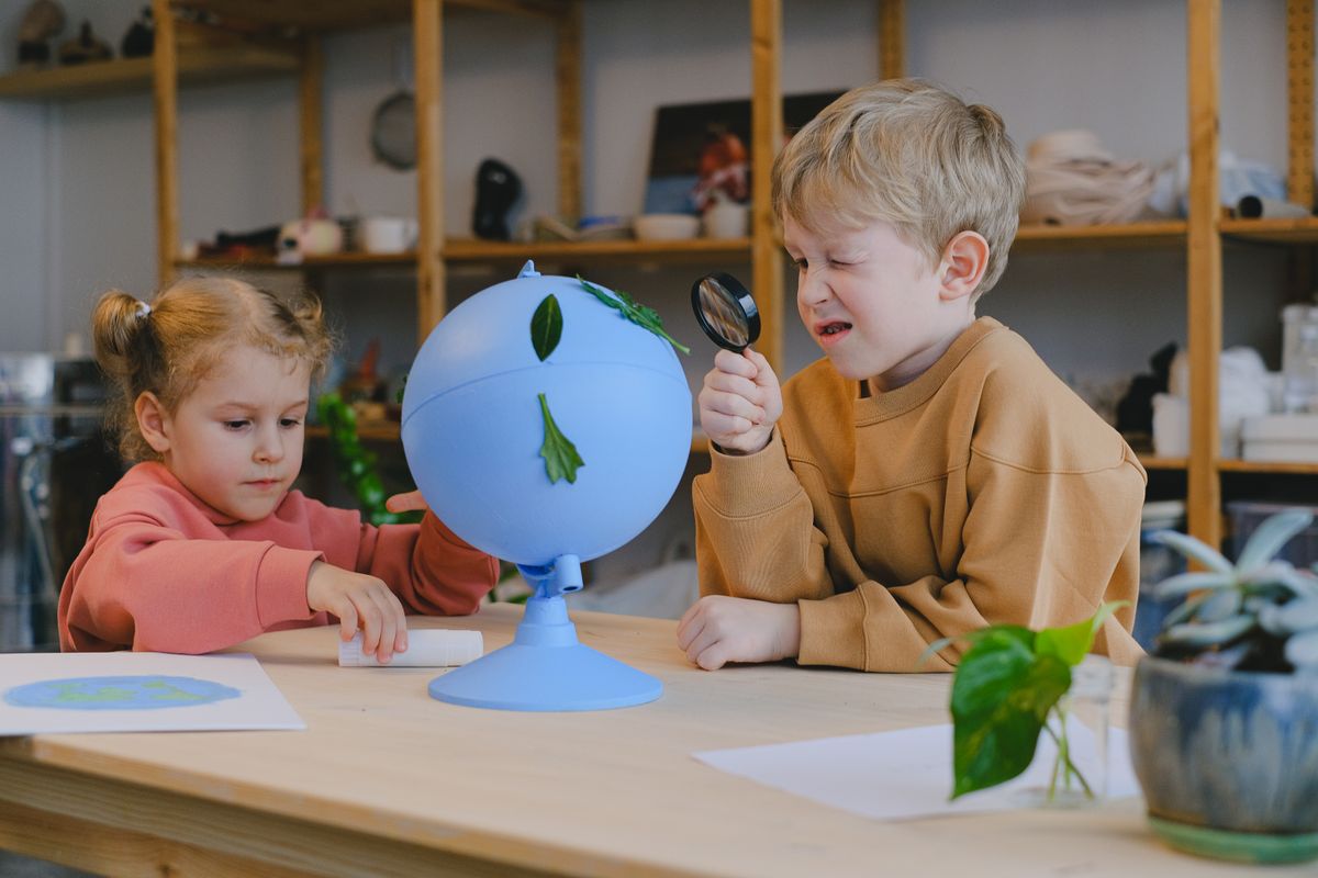 Bambini che osservano foglie su un mappamondo con la lente